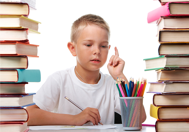 Portrait of cute youngster sitting among stacks of books and thinking while drawing