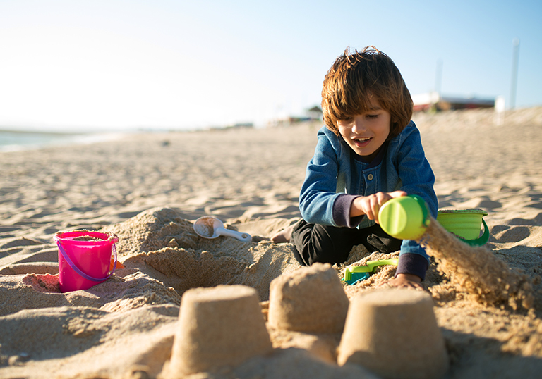 Boy building sandcastle. Schoolboy playing on beach on summer holidays. Child building sandcastle at sea. Family, vacation, outdoor activity concept
