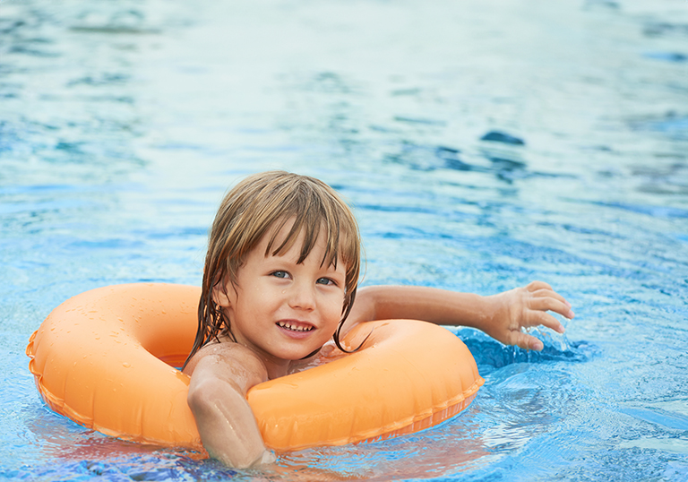 Smiling little boy practicing swimming in inflatable ring
