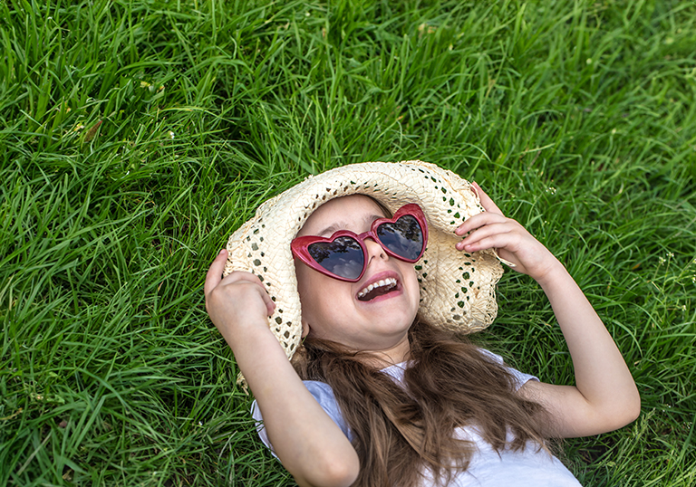 little girl laying in the grass with sunglasses and summer hat. summer time and sunny day