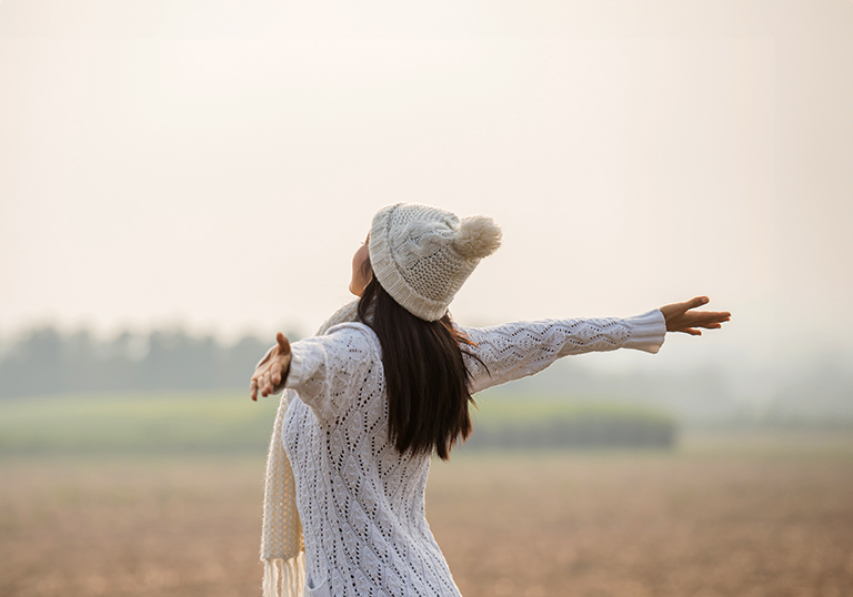 Happy woman enjoying in idyllic nature, celebrating freedom and rising her arms while standing toward the setting sun. Lifestyle and success concept.